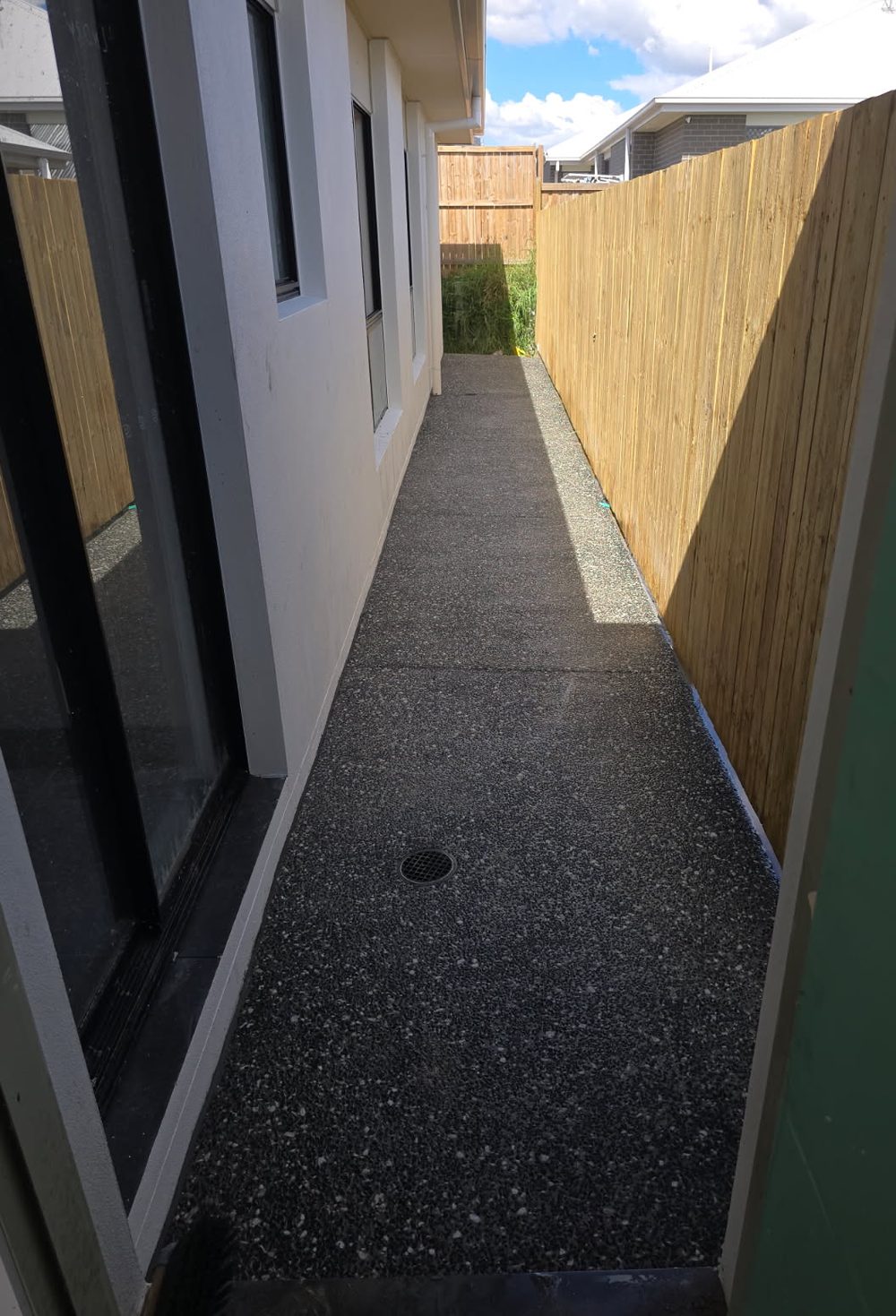 Dark exposed aggregate side path between a house and a timber fence